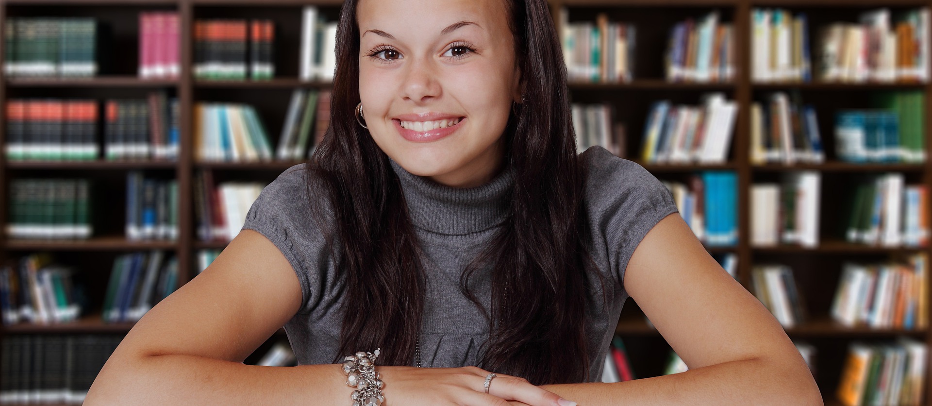 Teen female with brown hair in front of library bookshelves.