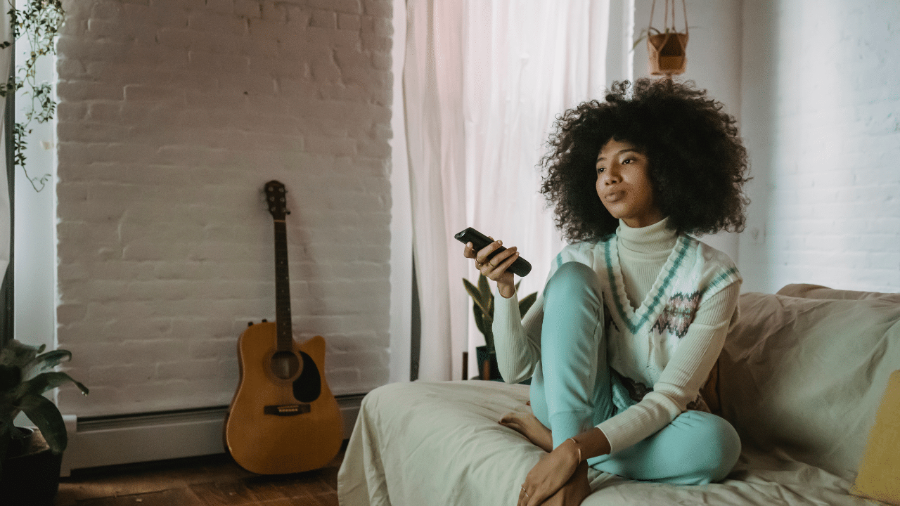 person on couch in apartment holds remote while watching cheap cable tv for low income