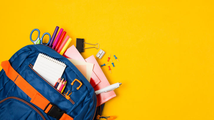 blue backpack on yellow background spills free school supplies across table
