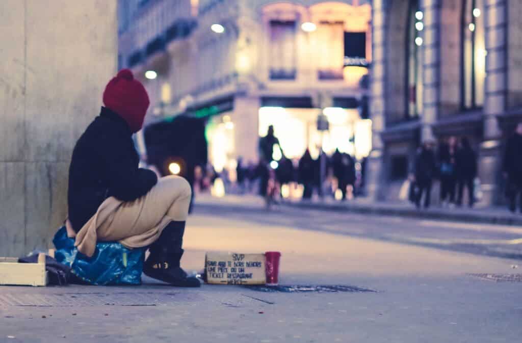 A homeless person sits at a public corner. Discussing the 4 types of homelessness