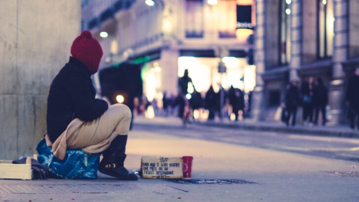 A homeless person sits at a public corner. Discussing the 4 types of homelessness