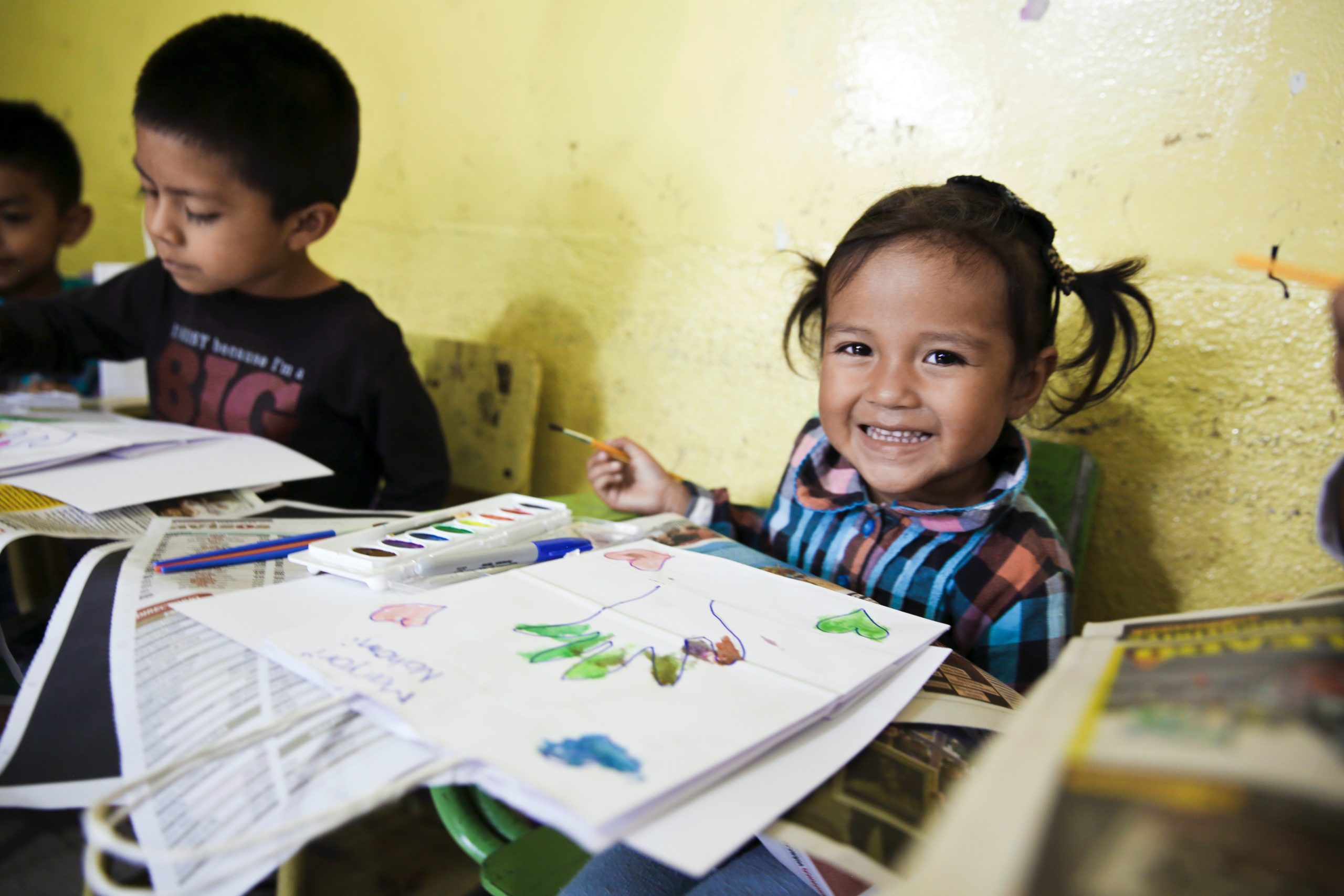 A boy of about four and a girl of about three painting with watercolors and smiling at a head start program