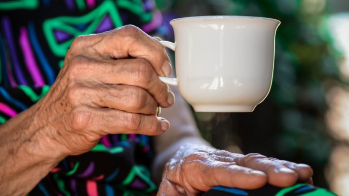 Hand of an elderly woman holding a white coffee cup in article about finding a senior citizens home