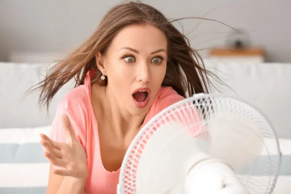 woman uses a fan to cool down a room without ac