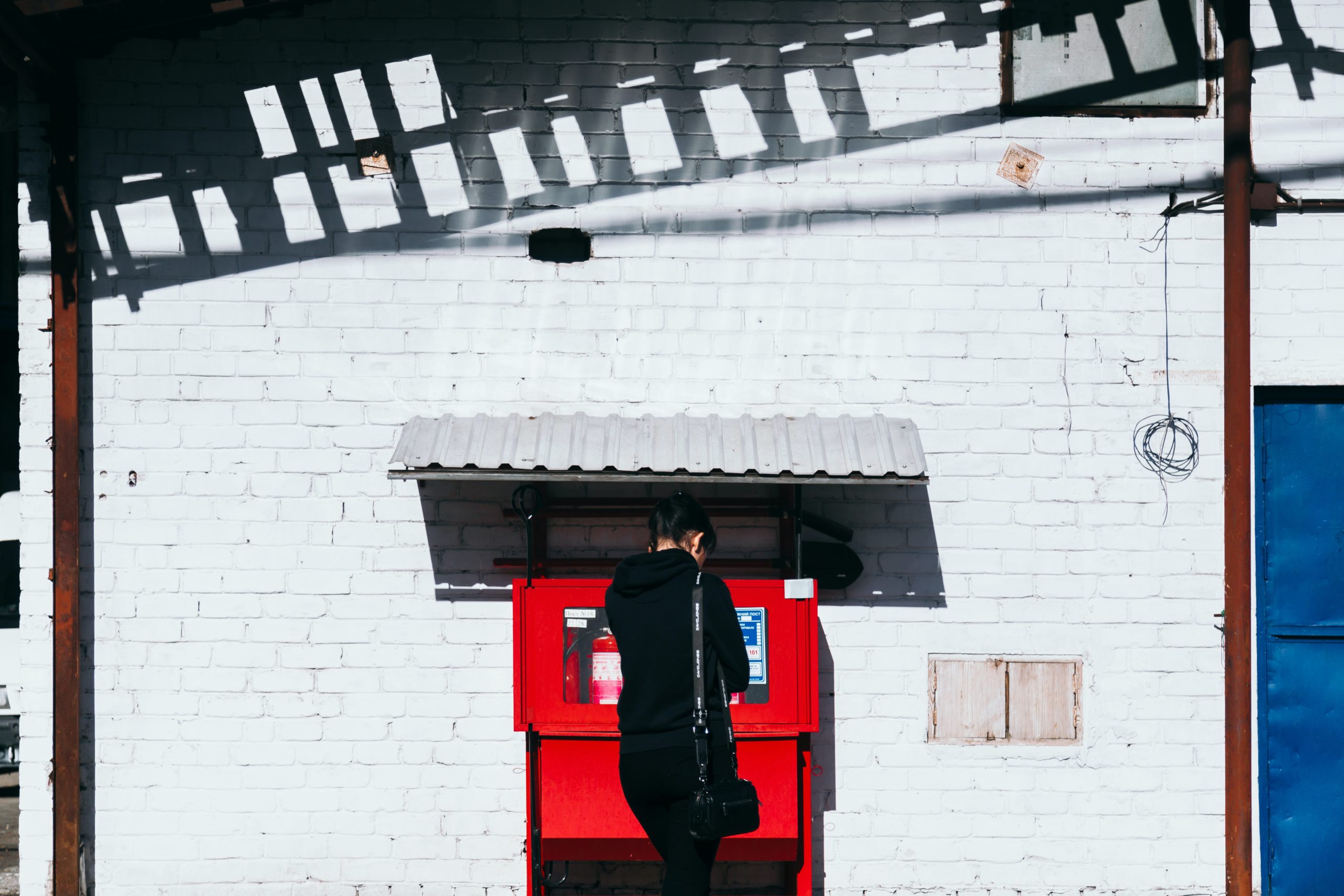 woman dressed in black using red atm machine set against white brick wall in article on how do i know if my ebt card has cash benefits?