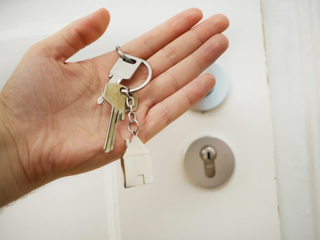 hand holding a set of keys on a keychain shaped like a house in article about can a landlord charge more than the security deposit