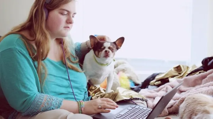 By Unsplash user Sharon McCutcheon. A woman pets a small brown and white dog as she works on her laptop.