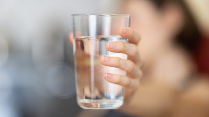 Hand holding a glass of drinking water against blurry background in article on LIHWAP Low Income Household Water Assistance Program