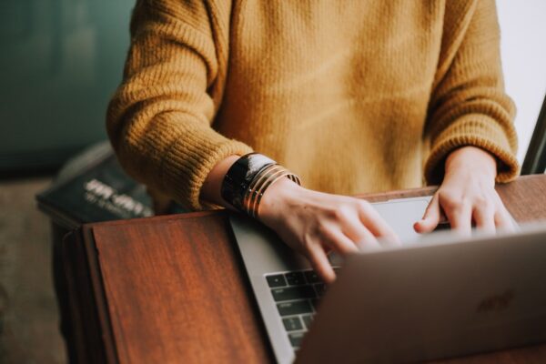 By Unsplash user Christin Hume. A person in a yellow sweater types on their laptop.