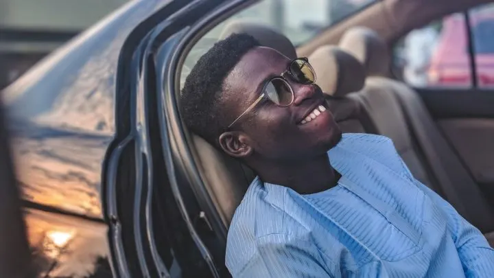 by Unsplash user Joshua Oluwagbemiga. A man with glasses leans back in his car, smiling.