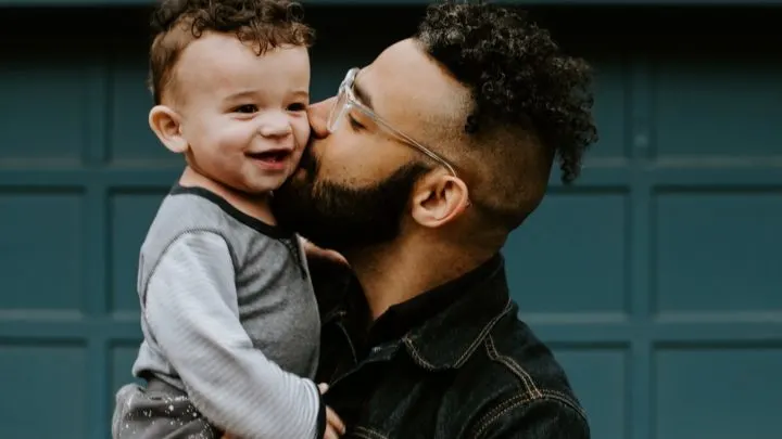By Unsplash user Kelly Sikkema. A bearded man kisses the cheek of smiling child he holds in his arms.