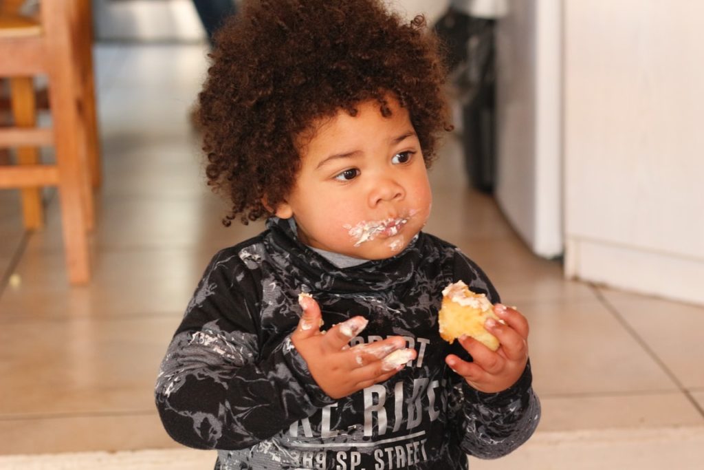 A toddler eating a piece of cake has icing smeared all over his face.