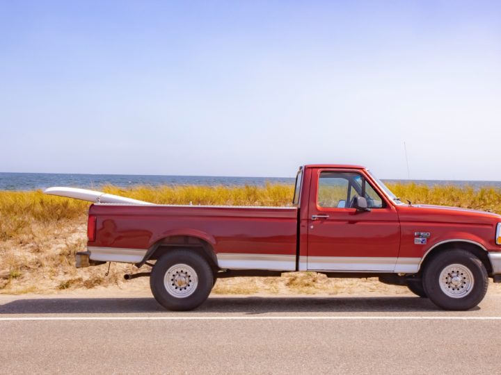 red truck driving past beach with a surfboard in the bed in article on California's consumer assistance program