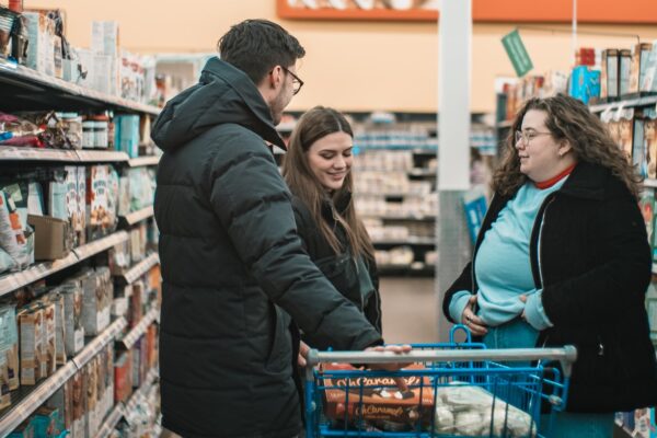 By Marie-Michèle Bouchard on Unsplash. A family stands in the aisles of a grocery store with their cart of goods.