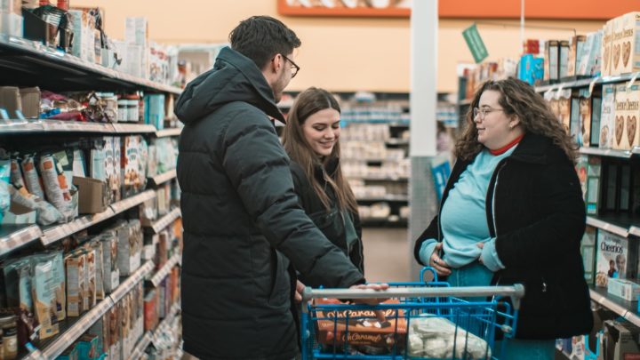 By Marie-Michèle Bouchard on Unsplash. A family stands in the aisles of a grocery store with their cart of goods.
