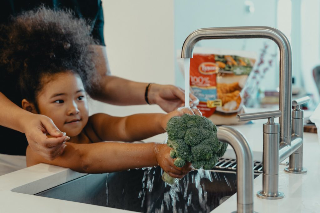 little girl washing broccoli in sink in article on financial assistance in Guam