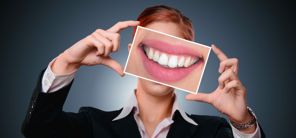woman holds image of teeth for low income dental clinics