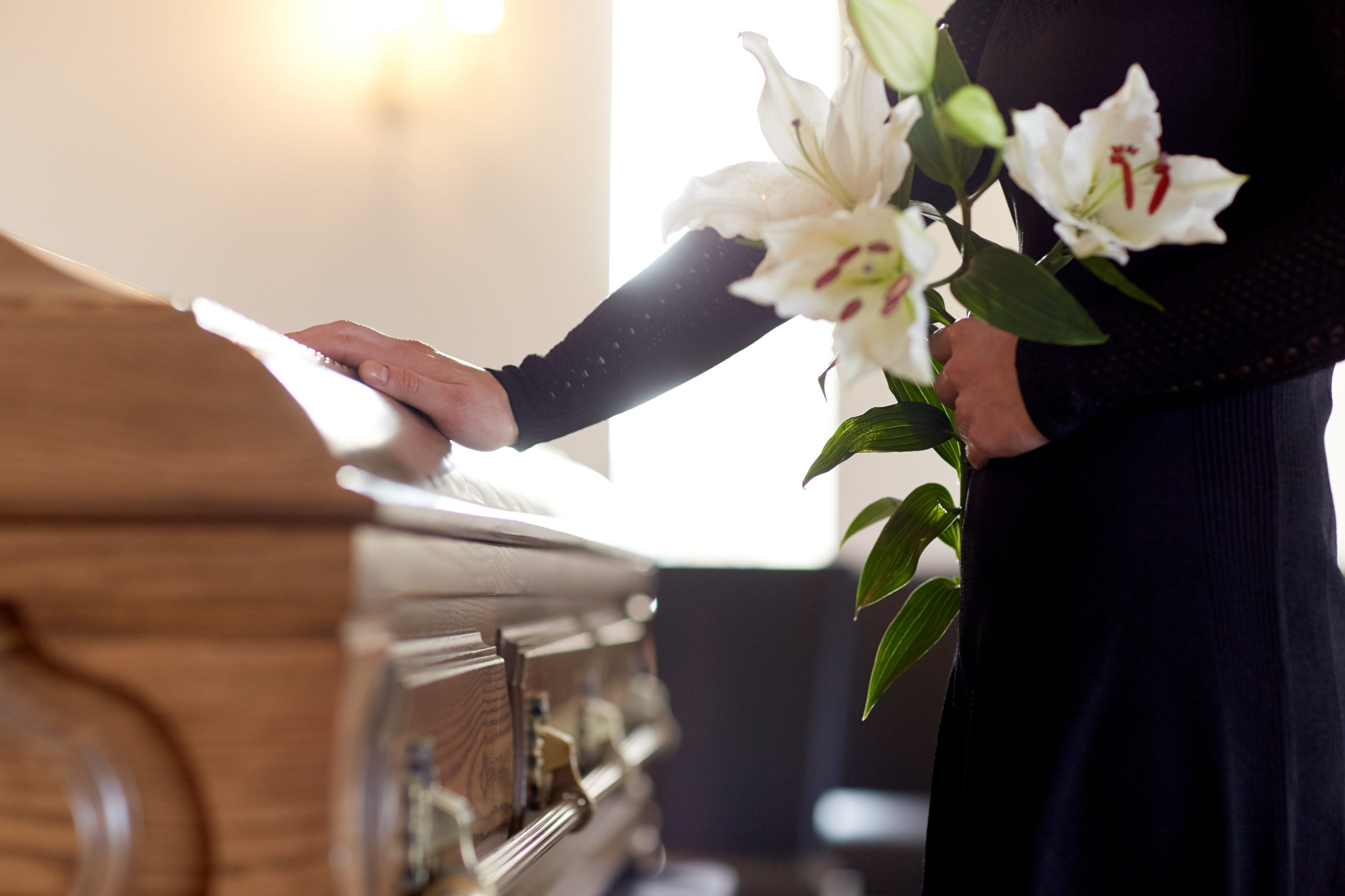 widow touches casket, holding flowers and worried about how to get help with funeral expenses