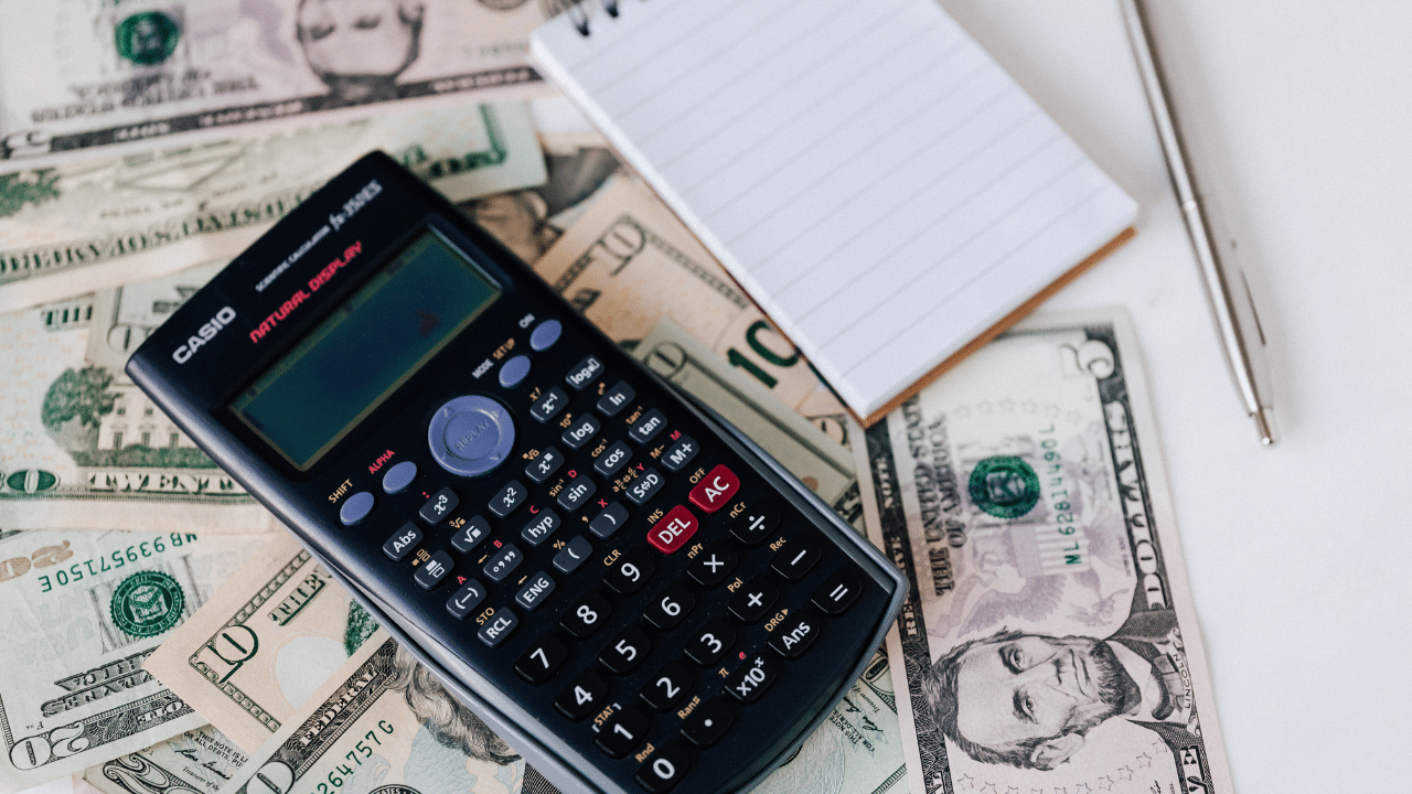 a calculator, notepad and pen are placed on top of a pile of small cash bills, representing area median income calculations so people can figure out what is the AMI in my area