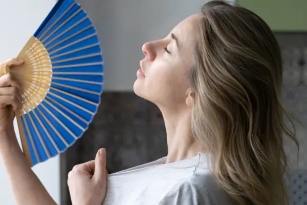 woman tries to stay cool by waving a fan while she waits for summer liheap application to go through