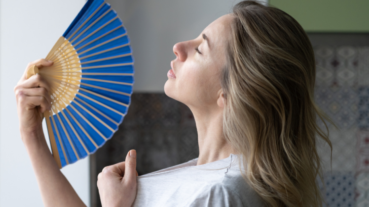 woman tries to stay cool by waving a fan while she waits for summer liheap application to go through