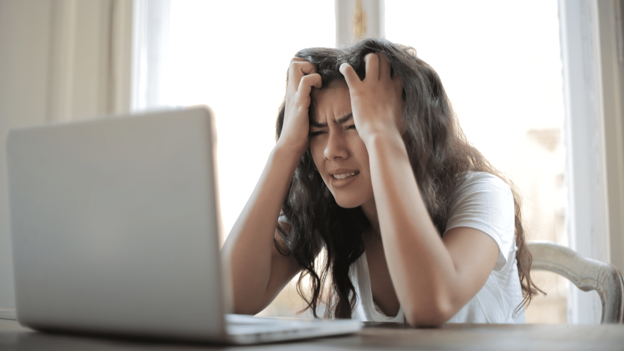 frustrated woman looks at laptop computer. Her hands are in her hair and her eyes are crinkled in frustration. She just learned that junk fees are back and hitting low income Americans hard.