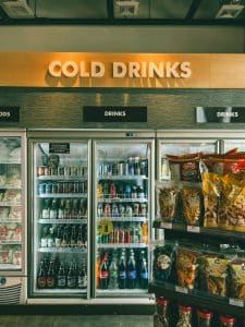 Beverage aisle with refrigerated drinks and snacks in a convenience store.